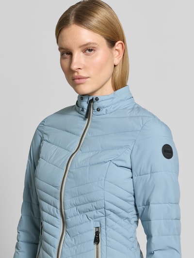 Vrouwenmodel draagt Slim Fit Jacke in Stepp-Optik van G.I.G.A. DX in lichtblauw, met afneembare capuchon, logo detail, ritssluiting, steekzakken met rits, gladde structuur, close-up bovenlichaam.