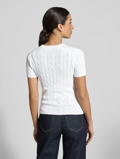 Modelka nosi Slim Fit Kurzarmpullover mit Label-Stitching od Polo Ralph Lauren, biała bawełna, optyka dzianiny, widoczna kieszeń na piersi, logo, krój slim fit, krótki rękaw, okrągły dekolt, elastyczne wykończenia, widok całej sylwetki od tyłu.