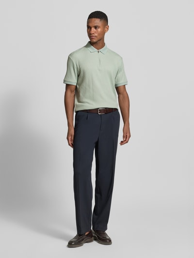 Męski model nosi Regular Fit Poloshirt mit Baumwoll-Anteil Modell 'FAVE' od SELECTED HOMME, gładki, krój regular fit, krótki zamek, krótki rękaw, mankiety ze ściągaczem, kołnierzyk polo, faktura prążkowana, zielony, spodnie ciemne, widok całej sylwetki z przodu