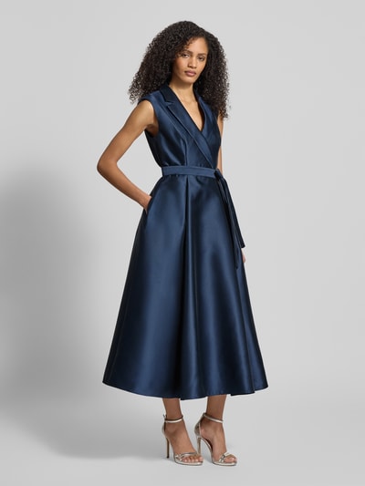 Frauenmodel trägt Cocktailkleid mit Reverskragen von Adrianna Papell in Dunkelblau, taillierter Schnitt, Taillengürtel, blickdichtes Unterkleid, Nahtreißverschluss, Rückenlänge 38 cm, Brustweite 39 cm, Ganzkörperansicht von vorne.