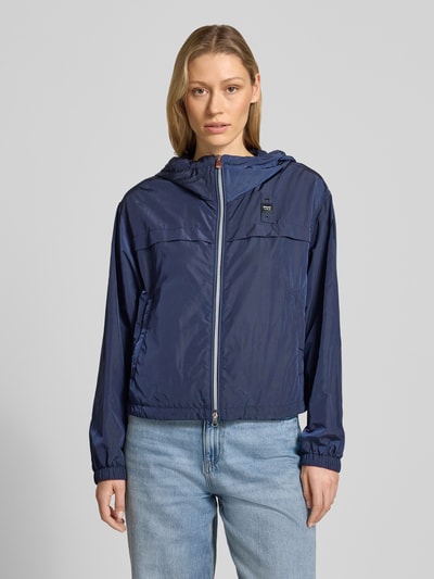 Frauenmodel trägt Trekking Jacke mit Kapuze Modell 'BURRAGE' von Blauer Usa in Dunkelblau, Zweiwege-Reißverschluss, Glanzoptik, Ganzkörperansicht von vorne.