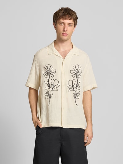 Männermodel trägt Relaxed Fit Freizeithemd aus reiner Baumwolle Modell 'JACKSON' von Only & Sons in Creme mit schwarzer Stickerei und Resortkragen, unifarbene Seersucker-Textur, durchgehende Knopfleiste, Kurzarm, Ganzkörperansicht von vorne.