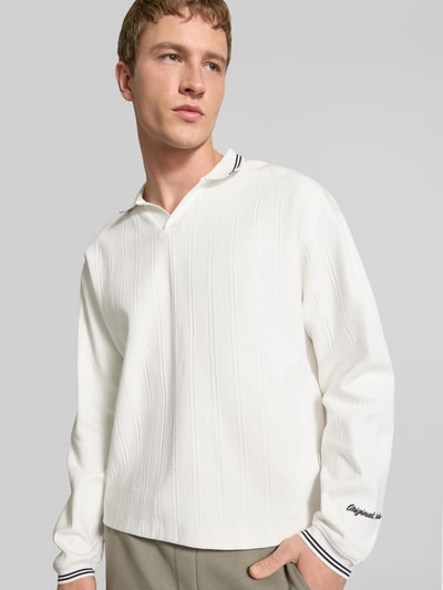 Männermodel trägt Strickpolo aus reiner Baumwolle Modell 'JORNIAGARA' von JACK & JONES, weiß mit Kontrast-Umlegekragen, Nahaufnahme Oberkörper. Lockere Passform, Label-Detail, elastische Ärmelabschlüsse, Rückenlänge Größe M 64 cm.
