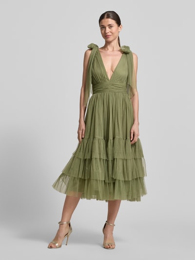 Frauenmodel trägt Knielanges Kleid mit Rüschenbesatz von LACE & BEADS in grünem Mesh, Taillierte Passform, V-Ausschnitt, Zierschleifen, Ärmelloses-Design, Knielänge, Rückenlänge bei Größe S 117 cm, Brustweite 32 cm, Ganzkörperansicht von vorne.