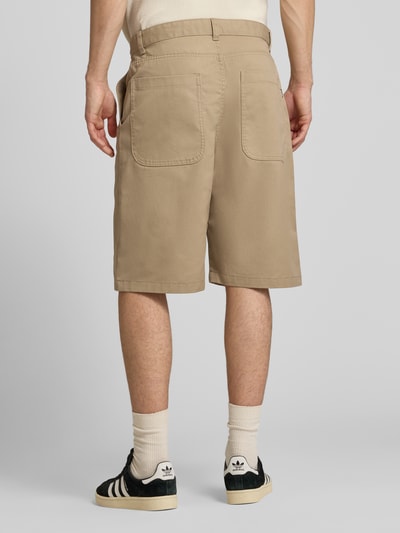 Męski model nosi Bermudas mit Eingrifftaschen od REVIEW, mieszanka bawełny, krój regular fit, wpuszczane i tylne kieszenie, beżowe, szerokość w rozmiarze M 45 cm, długość wewnętrzna nogawki 28 cm, pełny widok z tyłu.