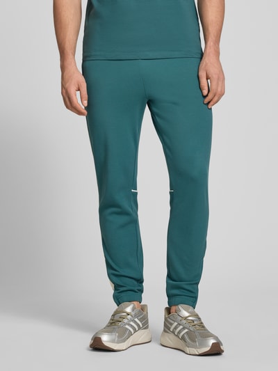 Männermodel trägt Slim Fit Tracksuit mit Logo-Stitching Modell 'Egeo' von SERGIO TACCHINI in Petrol, elastischer Baumwoll-Mix, Ganzkörperansicht von vorne.