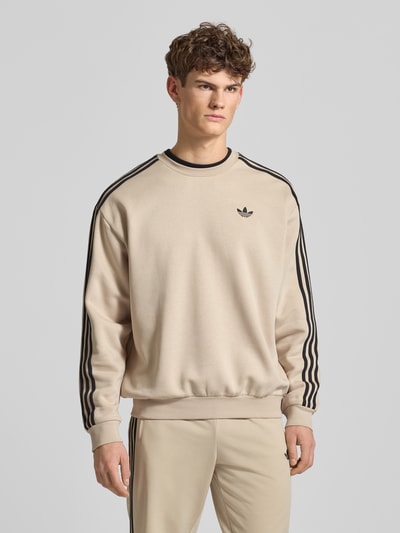 Męski model nosi Bluza z wyhaftowanym logo Sweatshirt mit Label-Stitching od adidas Originals, mieszanka bawełny, krój regular fit, prążkowane wykończenia, okrągły dekolt, długość tyłu 69 cm, długość rękawów 60 cm, widok całej sylwetki z przodu.
