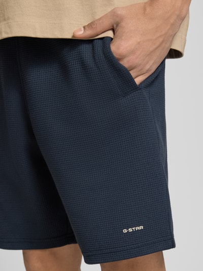 Männermodel trägt Straight Fit Shorts mit Strukturmuster von G-Star Raw im Elastischer-Material-Mix, Logo-Detail, Nahaufnahme Oberschenkel.