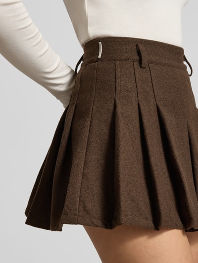 Frauenmodel trägt braunen Minirock mit Falten Modell 'Another Wool Skirt' von ANOTHER COTTON LAB, Material-Mix mit Viskose-Anteil, A-Linie, Nahaufnahme Oberkörper.