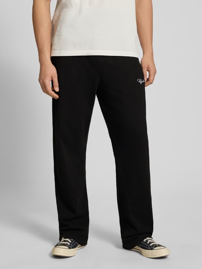Männermodel trägt Loose Fit Sweathose mit Logo-Stitching Modell 'Signar' von Pegador aus reiner Baumwolle, schwarze Farbe, Nahaufnahme Oberschenkel bis Füße, Kontext: Herren, Innenbeinlänge bei Größe M 83 cm.