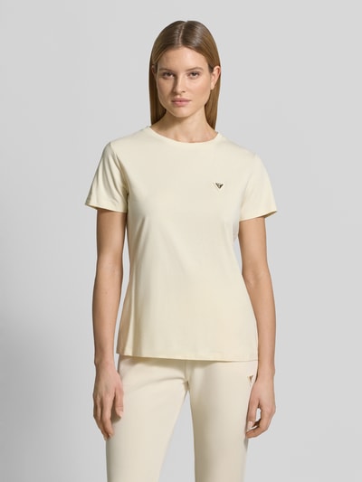 Modelka kobieca ma na sobie Regular Fit T-Shirt mit Logo-Applikation Modell 'Colette' od Guess Activewear w kolorze kremowym, elastyczna bawełna, krój regular fit, okrągły dekolt, długość tyłu w rozmiarze S: 60 cm, widok całej sylwetki z przodu