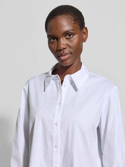 Frauenmodel trägt Bluse mit verlängertem Rücken Modell 'Berendine' von JOOP!, weiß, Baumwoll-Mix, Logo-Stitchings, Nahaufnahme Oberkörper.