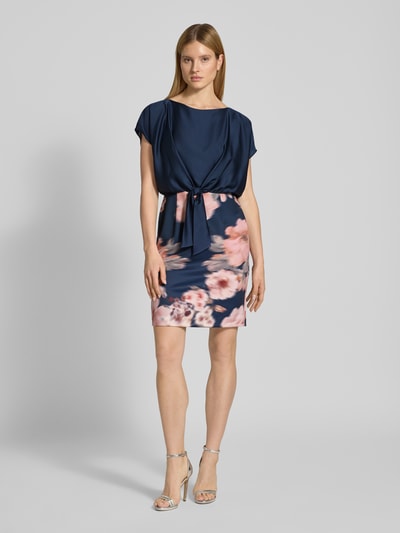Vrouwenmodel draagt knielanges Cocktailjurk met knoopdetail van SWING, materiaalmix met stretch, recht model, knielengte, ronde hals, bloemenprint. Ganzlichaamsaanzicht van voren.