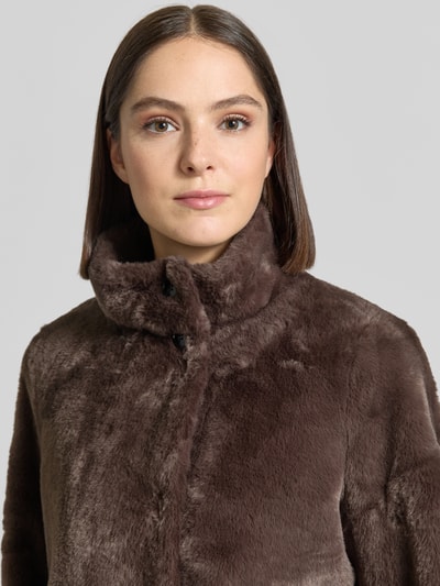 Frauenmodel trägt Jacke aus Kunstfell mit Eingrifftaschen von COMMA in Braun, sichtbare Knöpfe, weiche Textur, Nahaufnahme Oberkörper. Rückenlänge 54 cm, Schulterbreite 40 cm, Brustweite 56 cm, Ärmellänge 66 cm, Regular Fit, Stehkragen.