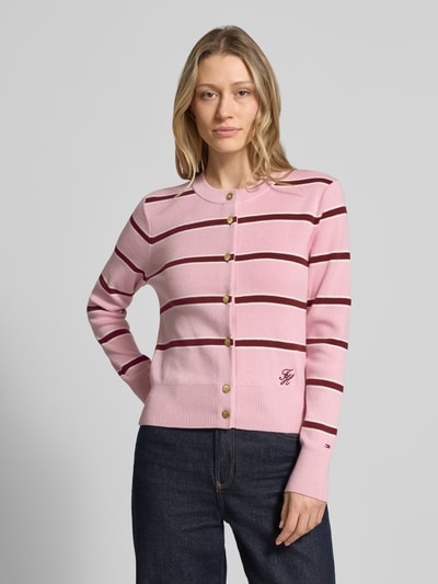 Kobiece model prezentuje Regular Fit Strickjacke aus reiner Baumwolle od Tommy Hilfiger, różowe paski, wyhaftowane logo, krój regular fit, wzór w paski, okrągły dekolt, długi rękaw, drobny splot, bawełna, efekt: wzór na całej powierzchni, listwa guzikowa, zakończenia prążkowane, Ganzkörperansicht von vorne.