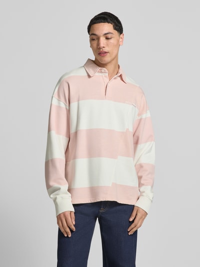 Męski model nosi Relaxed Fit Poloshirt aus reiner Baumwolle Modell 'Castelluccio' von Pegador w różowo-białe pasy, bawełna, kołnierzyk polo z zapięciem na guziki, prążkowane mankiety, logowana aplikacja, opuszczone ramiona, długość tyłu w rozmiarze M: 69 cm, ujęcie całej sylwetki z przodu.