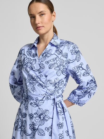 Modelka kobieca nosi 'Wickelkleid mit Stitchings und 3/4-Arm' od WHITE LABEL, linia a, sukienka midi, hafty, kołnierzyk koszulowy, dekolt w serek, wiązany pasek, rękaw o dł. 3/4, długość tyłu w rozmiarze 36: 116 cm, szerokość w rozmiarze 36: 48 cm, długość rękawów w rozmiarze 36: 45 cm, jasnoniebieski materiał z ciemnoniebieskim haftem kwiatowym, zdjęcie: zbliżenie na górną część ciała z przodu.