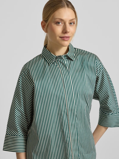 Frauenmodel trägt Regular Fit Hemdbluse mit durchgängiger Knopfleiste von Christian Berg Woman aus reiner Baumwolle, grün-weiß gestreift, Halbarm, Nahaufnahme Oberkörper.