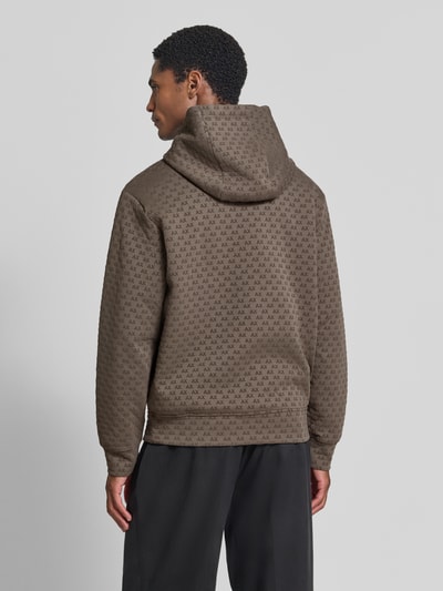 Männermodel trägt Regular Fit Hoodie aus Baumwoll-Mix von Armani Exchange mit Allover-Logo-Print in Braun, Ganzkörperansicht Rückansicht. Elastischer Baumwoll-Mix, Kapuze mit Tunnelzug, elastische Abschlüsse, Rückenlänge 66 cm, Ärmellänge 63 cm.