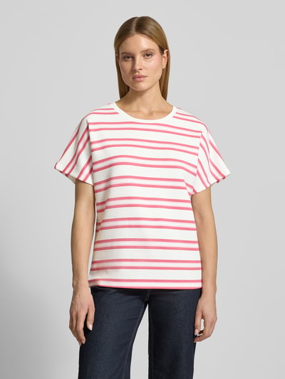 Kobiece model prezentuje damski t-shirt z mieszanki materiałów z domieszką modalu, krój relaxed fit, model 'BARNI' od Soyaconcept, okrągły dekolt, białe tło z różowymi i czerwonymi paskami, widok całej sylwetki z przodu.