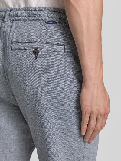 Mężczyzna nosi Regular Fit Chino aus Baumwoll-Mix od Tom Tailor, melanż, bawełniany materiał, tylne kieszenie, detal label patch, zapięcie na guzik i ukryty zamek, widok z tyłu – zbliżenie na biodro.
