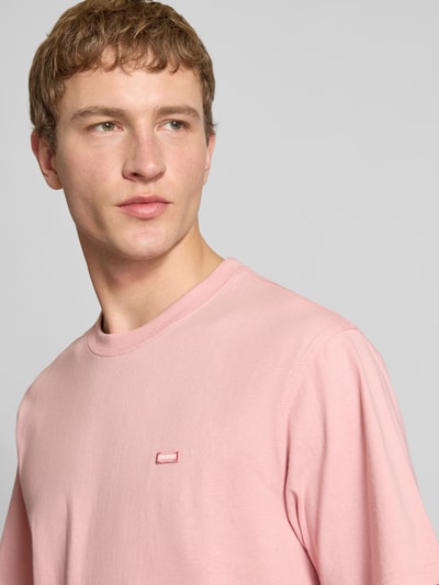 Männermodel trägt T-Shirt mit Label-Detail und Rundhalsausschnitt von Dickies in Rosa, Relaxed Fit, reine Baumwolle, Nahaufnahme Oberkörper.