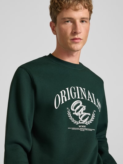 Männermodel trägt dunkelgrünes Sweatshirt mit Label-Print Modell 'FREDERIKSBERG' von JACK & JONES, Nahaufnahme Oberkörper, Baumwoll-Mix, Regular Fit.