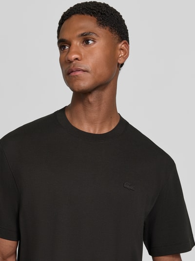 Männermodel trägt Regular Fit T-Shirt aus reiner Baumwolle von Lacoste in Schwarz, glatte Struktur, Nahaufnahme Oberkörper. Herren T-Shirt von Lacoste