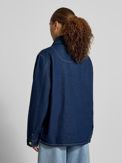 Frauenmodel trägt Jacke aus reiner Baumwolle in Denim-Optik Modell 'Edda' von LOLLYS LAUNDRY, Dunkelblau mit weißen Nähten, Paspeltaschen, lockerer Schnitt, Umlegekragen, Rückenansicht Ganzkörperansicht. Kontext: Damenjacke, Relaxed Fit, durchgehende Knopfleiste, Motiv-Stitching, Rückenlänge 69 cm, Schulterbreite 41 cm, Brustweite 56 cm, Ärmellänge 63 cm.