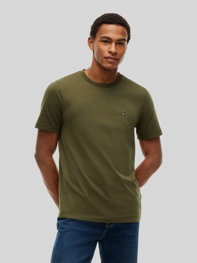 Męski model nosi Regular Fit T-Shirt aus reiner Baumwolle von Tommy Hilfiger w kolorze oliwkowym, gładka faktura, Ganzkörperansicht von vorne.