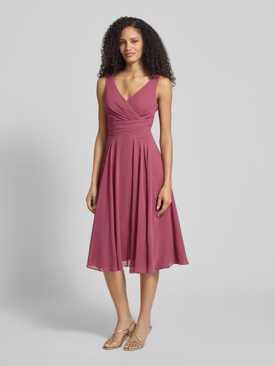 Modelka nosi Knielanges Cocktailkleid aus Chiffon mit V-Ausschnitt od TROYDEN COLLECTION, szyfon, krój taliowany, długość do kolan, dekolt V, długość tyłu w rozmiarze 36: 87 cm, szerokość w rozmiarze 36: 34 cm, długość rękawa w rozmiarze 36: 108 cm, kolor malinowy, widok całej sylwetki z przodu.