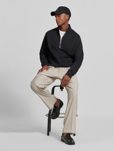 Männermodel trägt Regular Fit Troyer aus reiner Baumwolle Modell 'WAARLO' von ARMEDANGELS in Dunkelblau, helle Hose, schlichte Farben, Ganzkörperansicht von vorne. Herren Troyer von ARMEDANGELS.