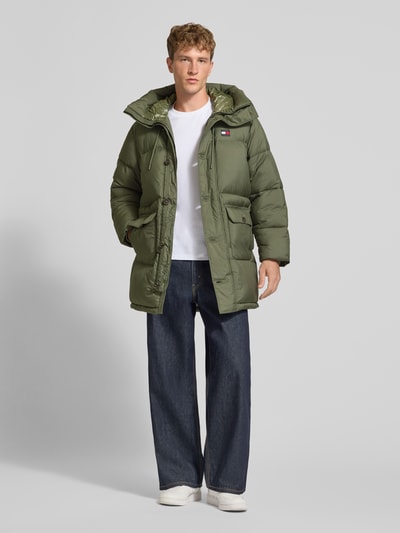 Männermodel trägt Parka mit Logo-Patch Modell 'WORKWEAR' von Tommy Jeans in Olivgrün, matte Struktur, Longline, Ganzkörperansicht von vorne