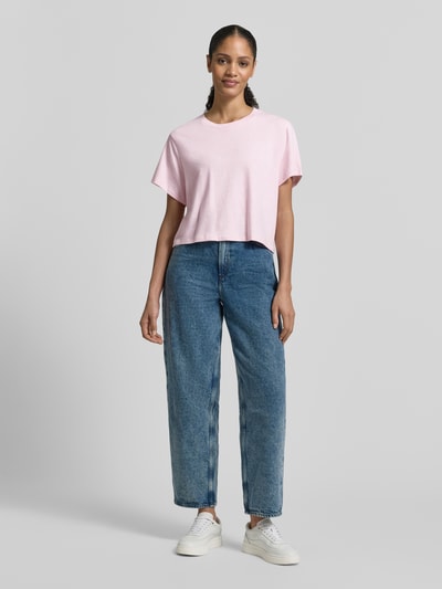 Frauenmodel trägt T-Shirt mit geripptem Rundhalsausschnitt von American Vintage, lockerer Schnitt, Rosa, kombiniert mit Jeans, Ganzkörperansicht von vorne.
