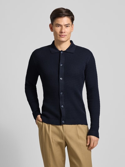 Männermodel trägt Strickjacke mit Strukturmuster Modell 'Yuris' von Cinque, dunkelblau, Knopfleiste, Polokragen, Ganzkörperansicht von vorne.