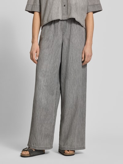Kobiece model prezentuje spodnie materiałowe Wide Fit Stoffhose mit Rüschenbesatz Modell 'Dwindle' od Drykorn z czystej bawełny, krój wide fit, obszycie falbanami, elastyczny pas z tunelem, wpuszczane kieszenie, szerokość w rozmiarze 27/34: 37 cm, długość wewnętrzna nogawki 82 cm, odcień szarości, miękka tekstura, całość z przodu.