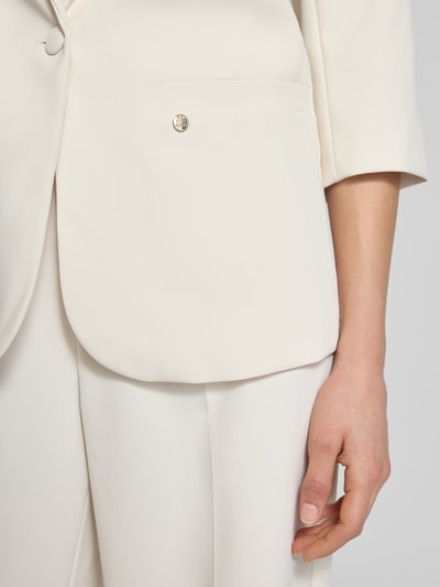 Frauenmodel trägt Regular Fit Blazer mit 3/4-Arm Modell 'Junie Miley' von MOS MOSH in Creme, glatte Textur, Nahaufnahme Oberkörper, Fokus rechter Arm und Hüfte.