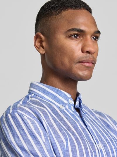 Męski model trägt Slim Fit Freizeithemd aus reinen Leinen von Christian Berg Men, kołnierzyk typu button down, listwa guzikowa, krój slim fit, z długim rękawem, sportowe mankiety, niebiesko-białe pionowe pasy, lekka faktura, szersze białe i cieńsze niebieskie linie, długość tyłu w rozmiarze M: 79 cm, szerokość w rozmiarze M: 48 cm, długość rękawów w rozmiarze M: 65 cm, nahaufnahme oberkörper.