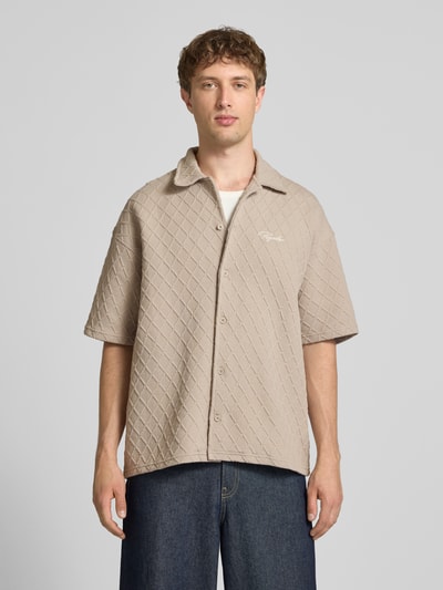 Männermodel trägt Modern Fit Freizeithemd mit Logo-Stitching Modell 'Jovren' von Pegador im Strukturmuster, Kentkragen, Knopfleiste, Material-Mix, beige, Ganzkörperansicht von vorne.