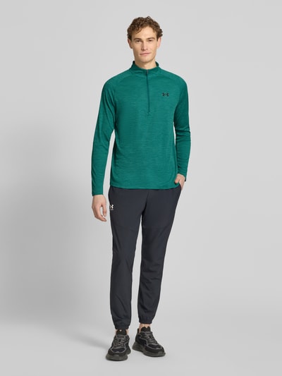 Mannemodel draagt Sweatshirt mit kurzem Reißverschluss und Logo-Print van Under Armour in groen met logoprint, recht model, opstaande kraag, ruglengte maat M 74 cm, mouwlengte maat M 64 cm, ganzkörperaanzicht van voren.