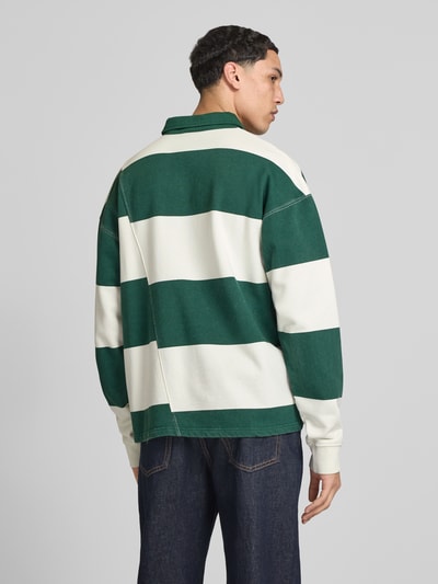 Mężczyzna nosi Relaxed Fit Poloshirt aus reiner Baumwolle Modell 'Castelluccio' von Pegador, szerokie zielono-białe pasy, wyhaftowane logo, oversize, kołnierzyk polo z listwą guzikową, ściągacze na rękawach, długość tyłu w rozmiarze M: 69 cm, widok całej sylwetki z tyłu.