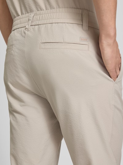 Männermodel trägt Tapered Chino mit Tunnelzug von BOSS Orange in Beige, unifarbene Struktur, seitliche Taschen, Detailaufnahme Rückansicht