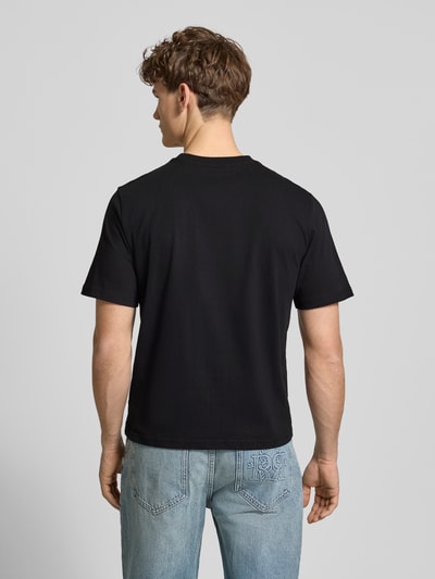 Männermodel trägt Basic T-Shirt mit kleinem Logo-Patch auf der Brust von REVIEW in Schwarz, reine Baumwolle, gerader Schnitt, Ganzkörperansicht Rückansicht.