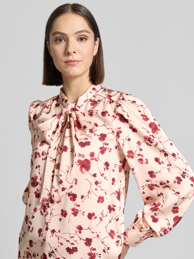 Vrouwenmodel draagt Regular Fit Schluppenbluse im Allover-Look van Christian Berg Woman Selection in lichtroze met rode bloemenprint, satijnachtige textuur, dames Schluppenbluse, ruglengte 62 cm, mouwlengte 64 cm, nahaufnahme bovenlichaam.