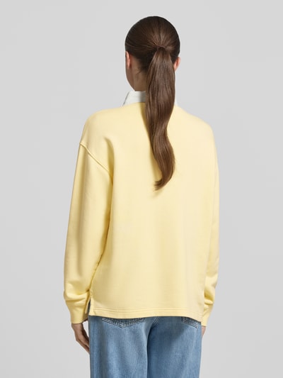 Frauenmodel trägt Longsleeve mit Polokragen und kurzer Knopfleiste von Gant, hellgelb, Baumwoll-Mix, Loose-Fit, Rückenlänge 63 cm, Ganzkörperansicht Rückansicht.