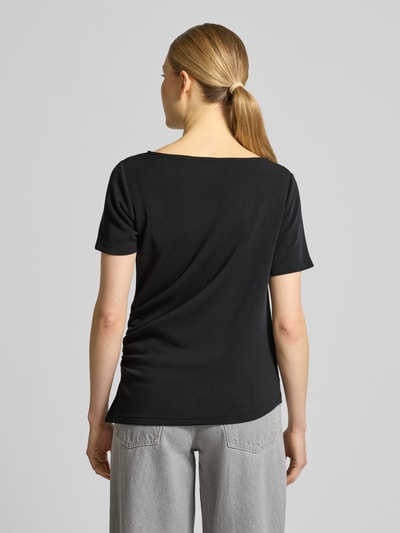 Modelka nosi damski t-shirt w asymetrycznym kroju, model 'Helle' od My Essential Wardrobe, mieszanka materiałów z dodatkiem wiskozy, okrągły dekolt, czarny kolor, drapowania, długość tyłu w rozmiarze S: 60 cm, widok całej sylwetki z tyłu.