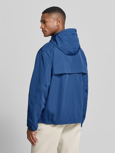 Männermodel trägt Regular Fit Regenjacke mit Logo-Stitching van Polo Ralph Lauren, look: effen, lange mouw, capuchon met tunnelkoord, tweewegritssluiting, rompzoom met tunnelkoord, steekzakken, merkstitching, kleur blauw, ganzkörperansicht rückansicht.