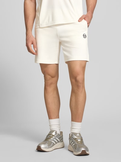 Männermodel trägt Shorts mit Logo-Stitching Modell 'EGEO' von SERGIO TACCHINI in Offwhite, lockerer Schnitt, sichtbarer Kordelzug, Nahaufnahme Oberschenkel, Kontext: Herren Shorts aus Baumwoll-Mix mit Stretch, seitliche Taschen, elastischer Bund, Größe M Bundweite 40 cm, Innenbeinlänge 20 cm.