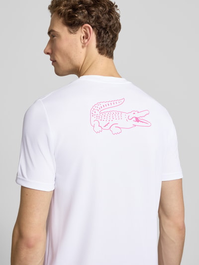 Männermodel trägt weißes Regular Fit T-Shirt mit UV-Schutz 50+ von Lacoste Sport, pinker Logo-Print, glatte Piqué-Struktur, Ganzkörperansicht Rückansicht.