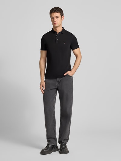 Männermodel trägt Slim Fit Poloshirt mit Stretch-Anteil von Tommy Hilfiger in zwart, korte mouwen, katoenen-elastaan mix, ganzkörperansicht von vorne.